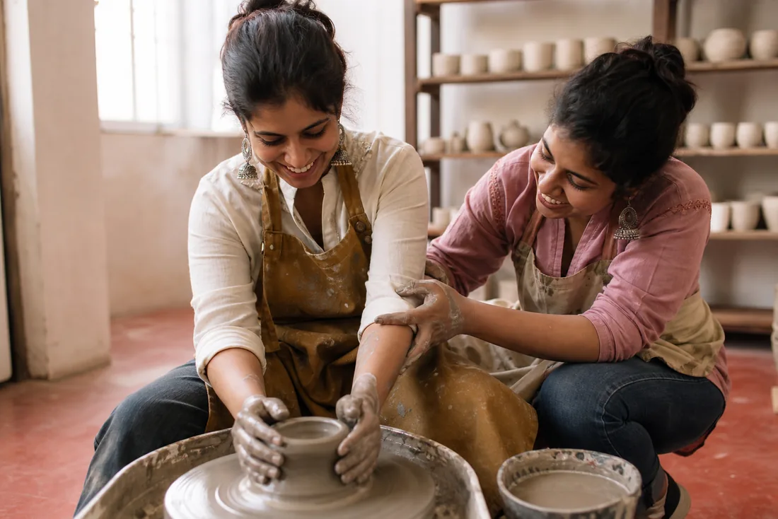 Two women working at a wheel in a pottery studio.
